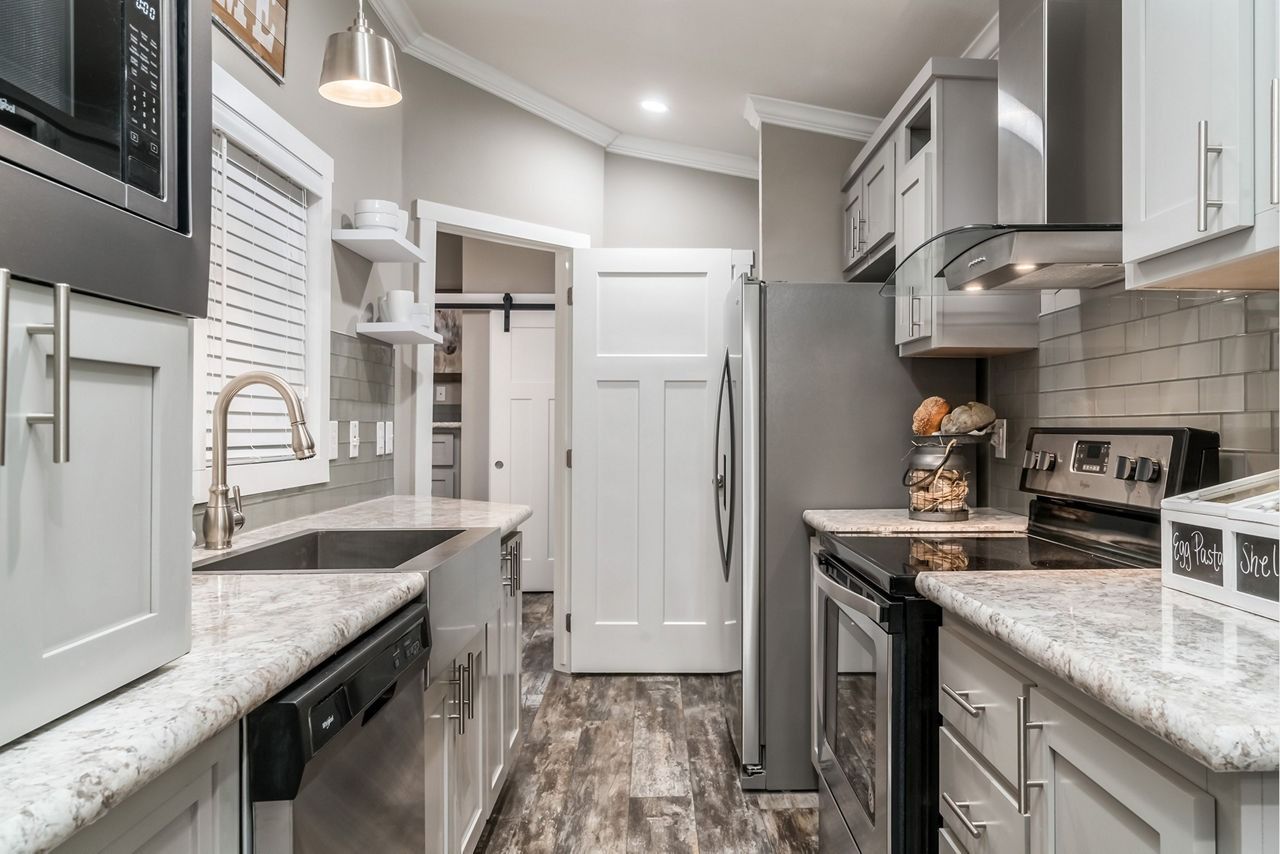 Compact gray kitchen with stainless appliances, white cabinets, granite counters, and wood-look flooring.