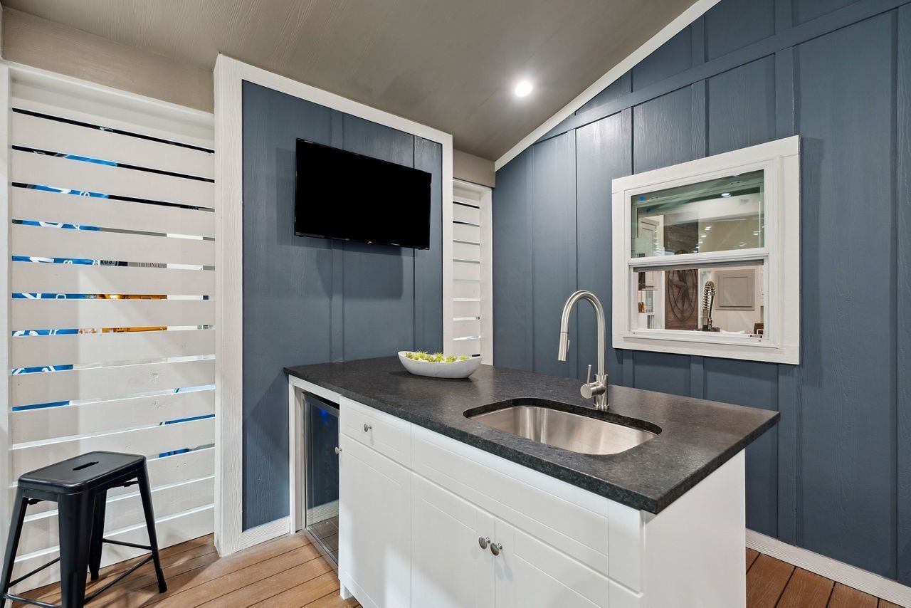 Modern kitchen with white cabinets, dark countertop, sink island, wall-mounted TV, and striped window shades