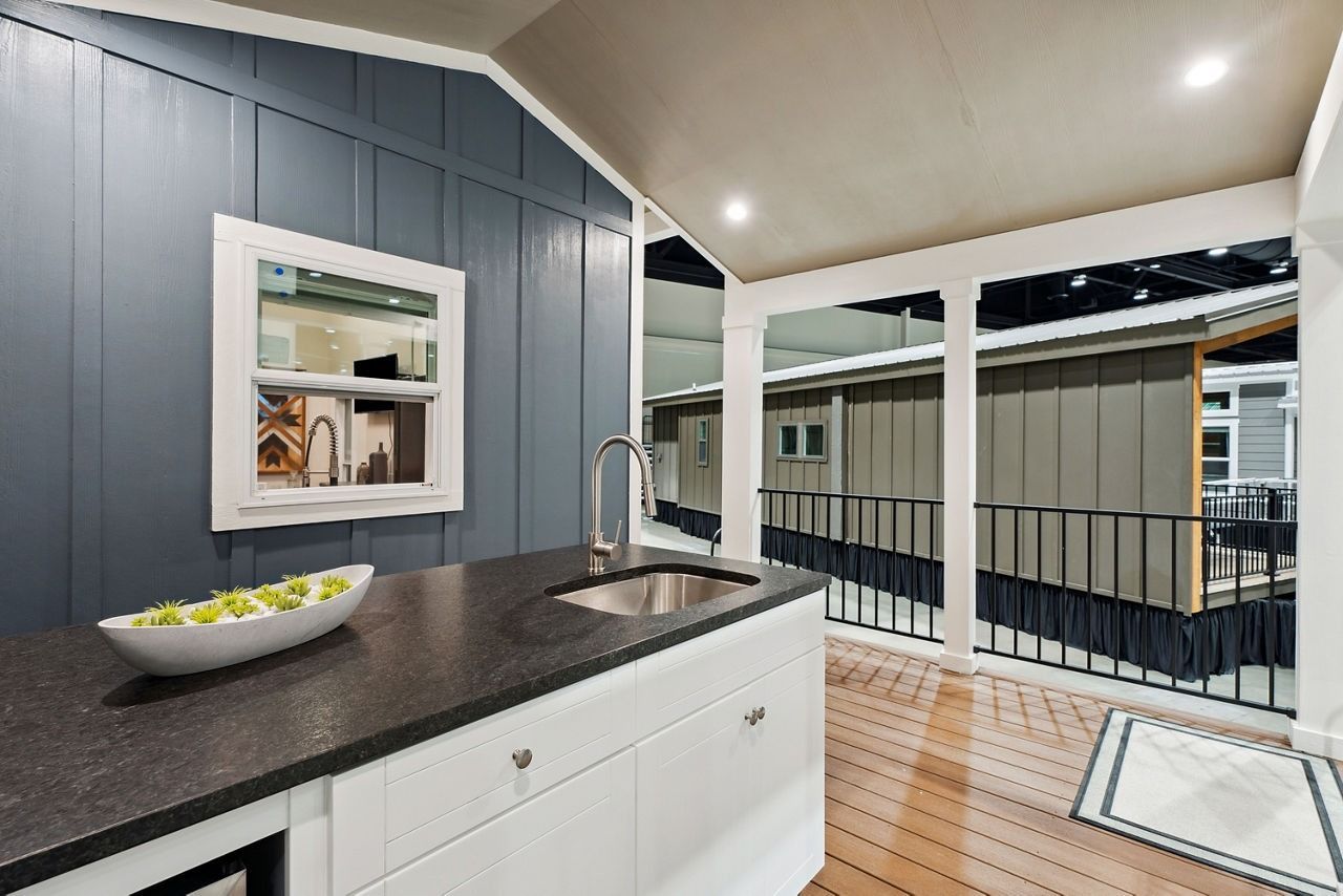 Modern kitchen with gray walls, black countertop, white cabinets, and a view into a sunroom.