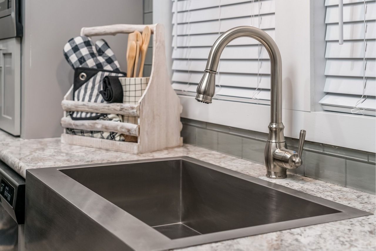 Modern kitchen sink with stainless steel faucet, gray countertop, and white window blinds