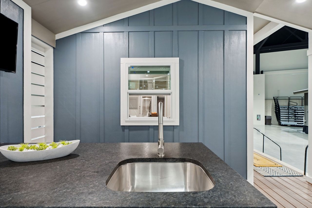 Kitchen sink with dark countertop, blue paneled walls, and a pass-through window to another room.