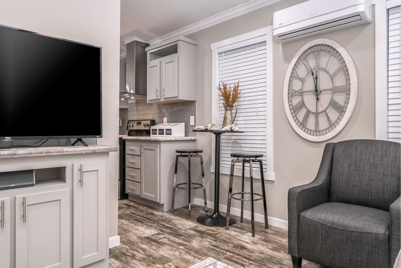 Cozy living room with gray chair, large wall clock, TV, and small breakfast bar with stools