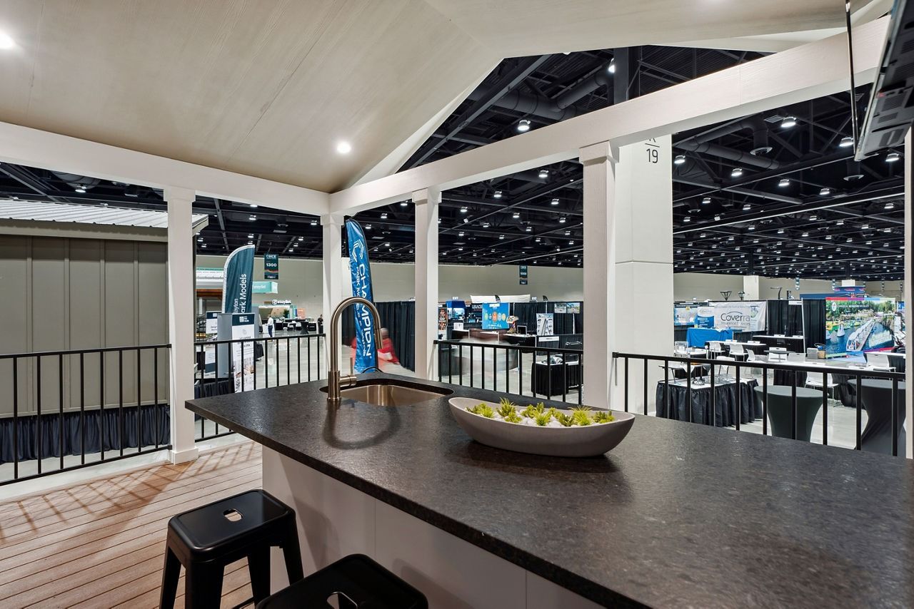 Indoor conference lounge with bar counter, stools, and a bowl of flowers under bright event hall lighting