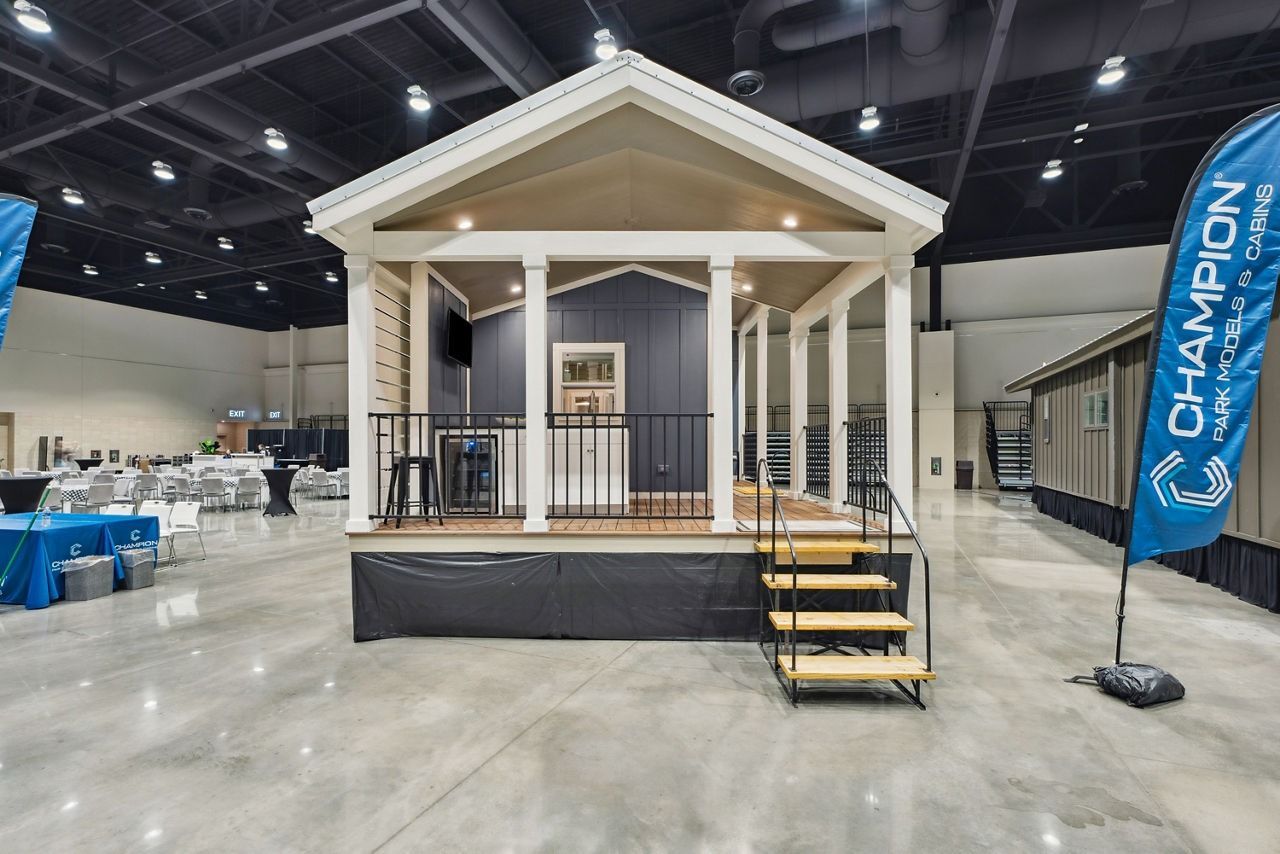 Small white porch display with steps inside an expo hall, flanked by a blue “Champion” banner.