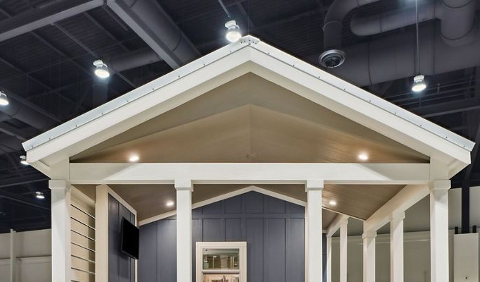 Indoor display of a small gray house facade with white trim and a peaked roof at an exhibition hall
