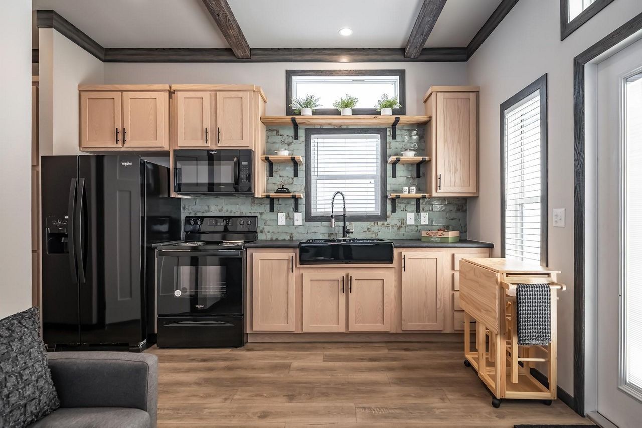 Small modern kitchen with light wood cabinets, black appliances, and a window over the sink