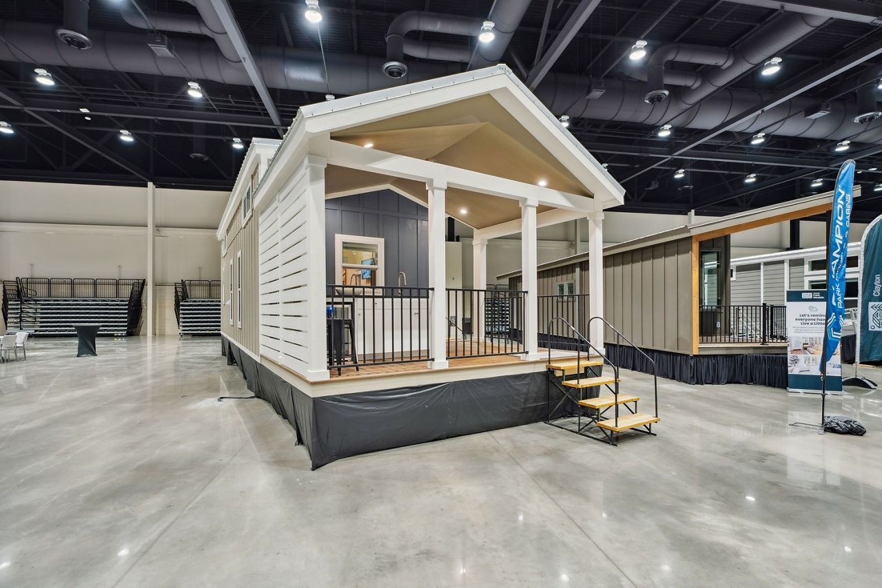 Tiny white house display with porch and steps inside a large exhibition hall