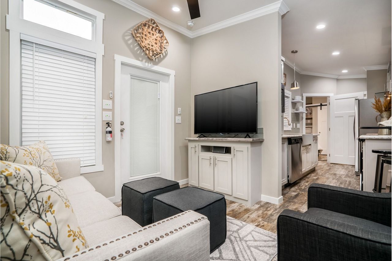Modern living room with white sofa, black ottomans, TV, and a doorway with blinds