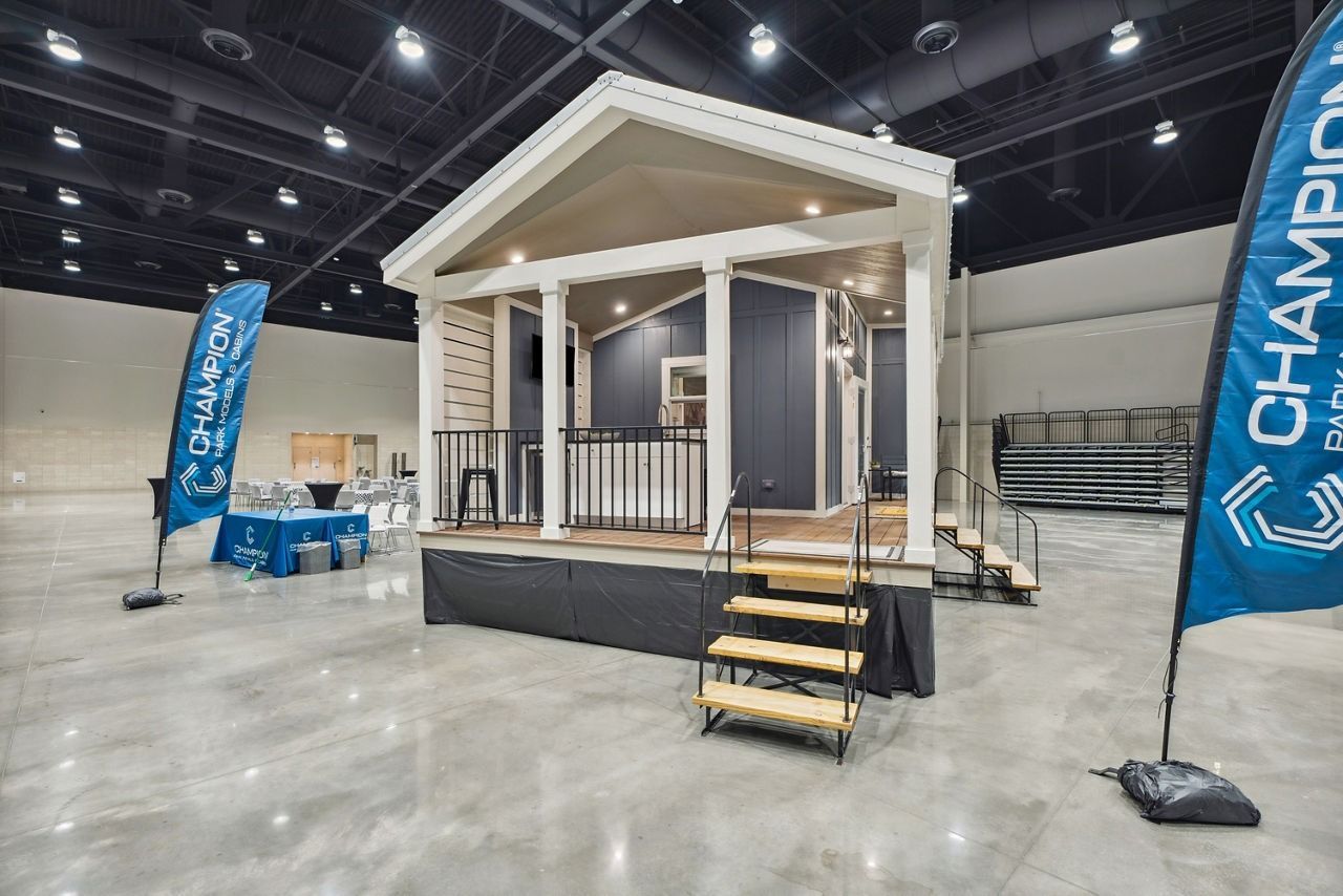 Indoor trade show booth with a small white porch display and blue Champion flags