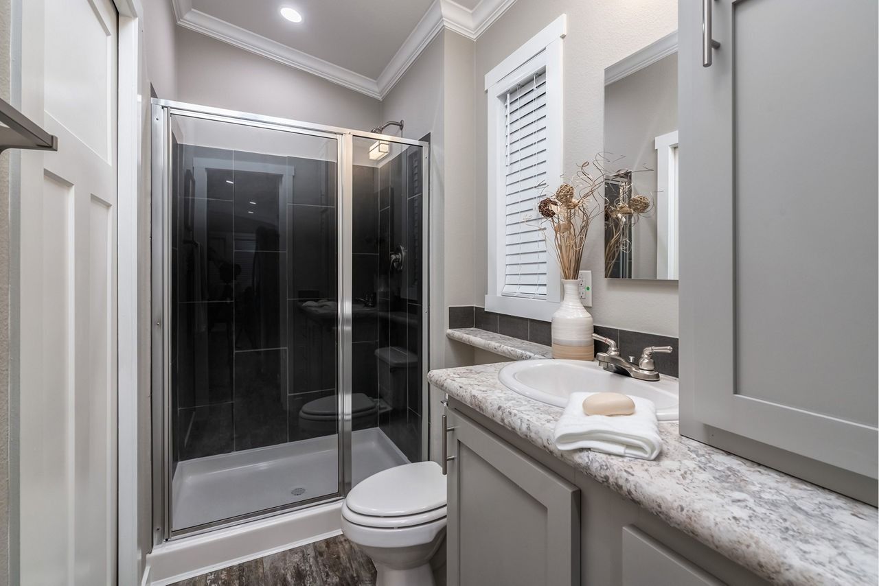 Modern bathroom with glass shower, white toilet, and granite vanity counter with sink and mirror.