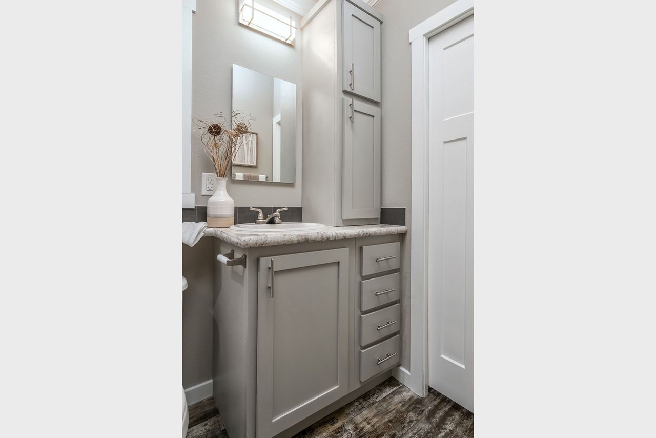 Small bathroom vanity with mirror, gray cabinets, and white walls in a narrow space