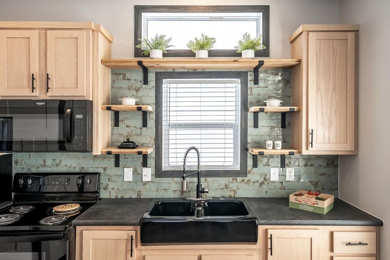 Bright kitchen with black countertops, light wood cabinets, window shelves, and potted plants above the sink