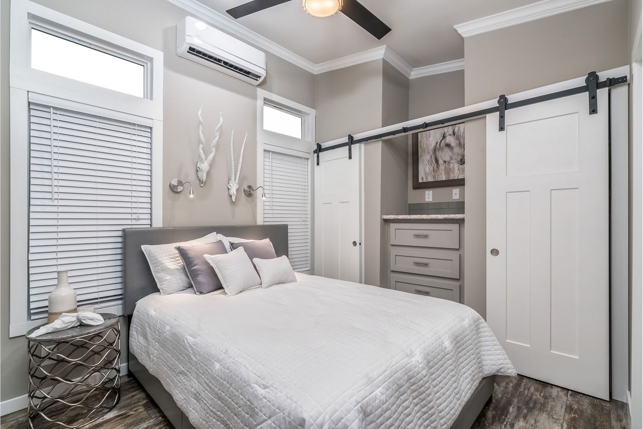 Modern bedroom with gray walls, white barn doors, and a bed with patterned bedding beneath tall windows