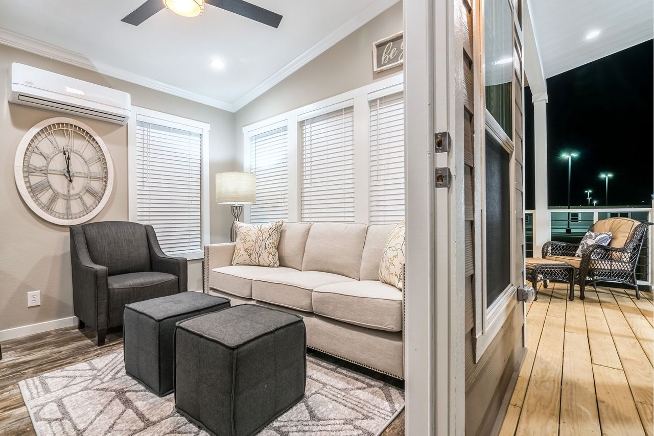 Cozy living room with gray armchair, beige sofa, wall clock, and open door to a lit deck at night