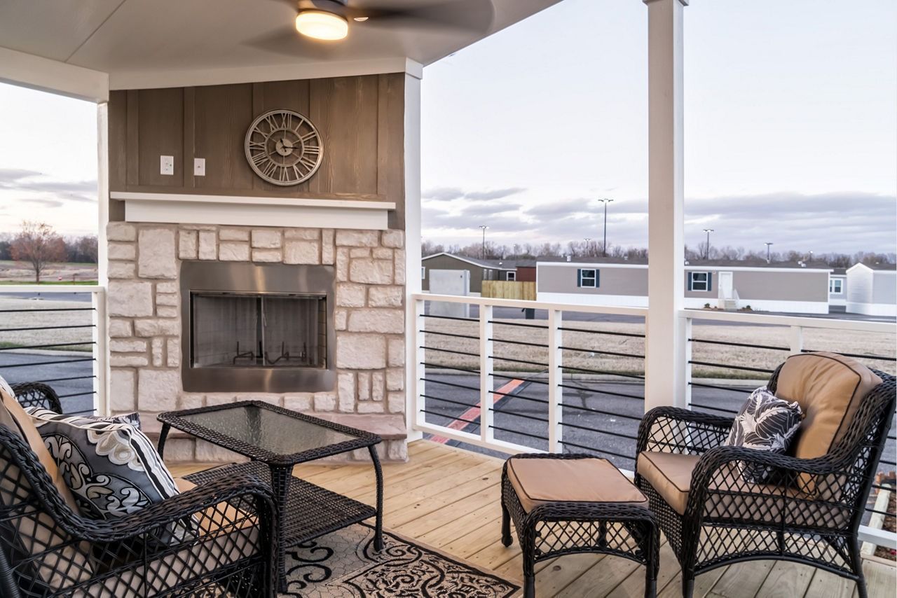 Covered patio with stone fireplace, wicker seating, and a view of a snowy landscape.