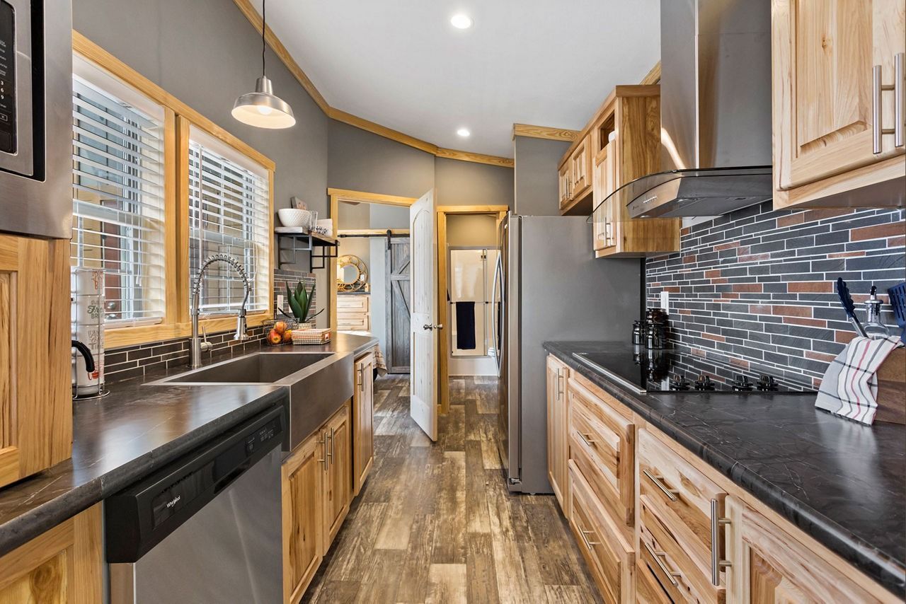 Modern kitchen with wood cabinets, black countertops, stainless steel appliances, and tiled backsplash.