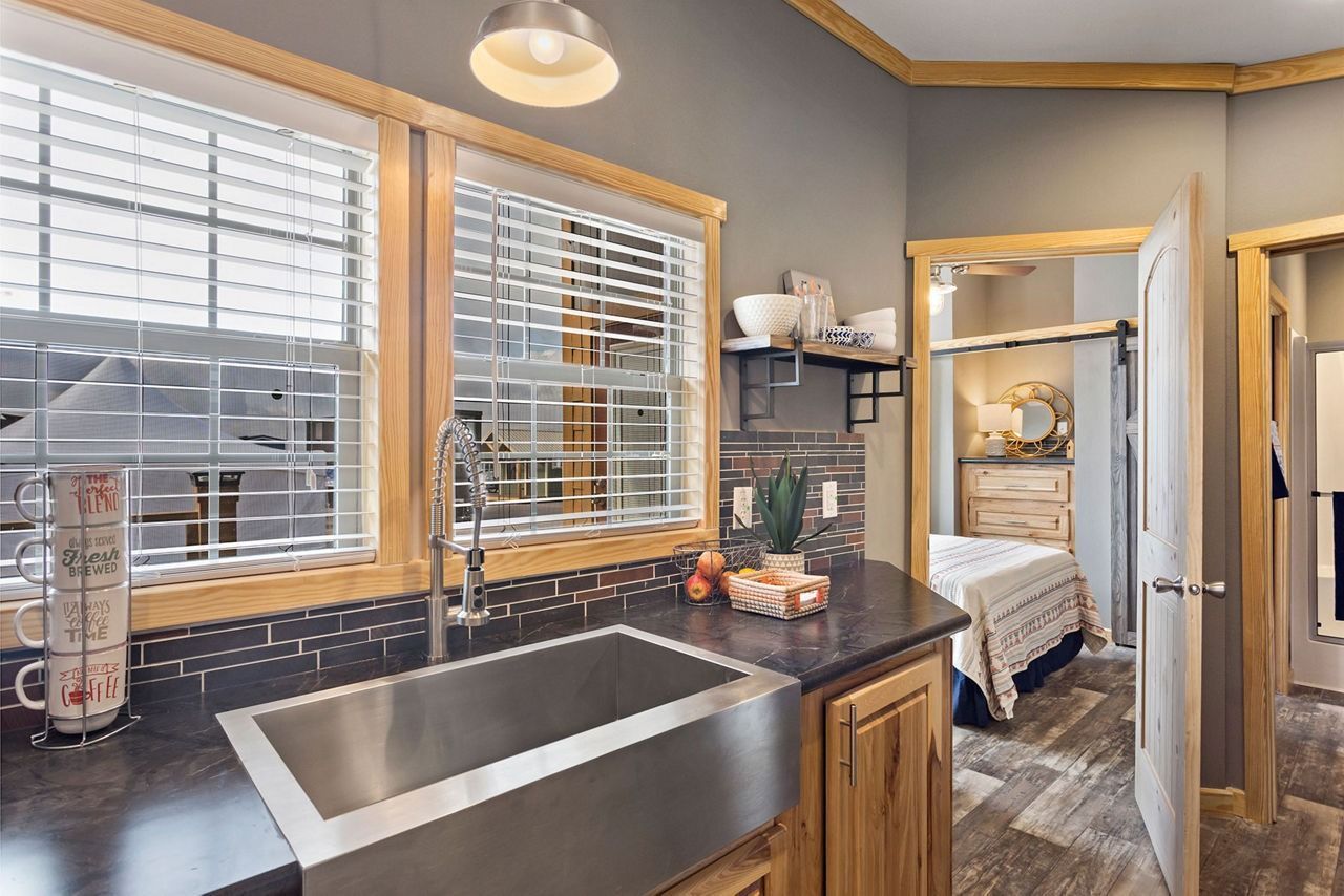 Modern kitchen with stainless sink, black countertops, wood cabinets, and a glimpse of a bedroom through open doors