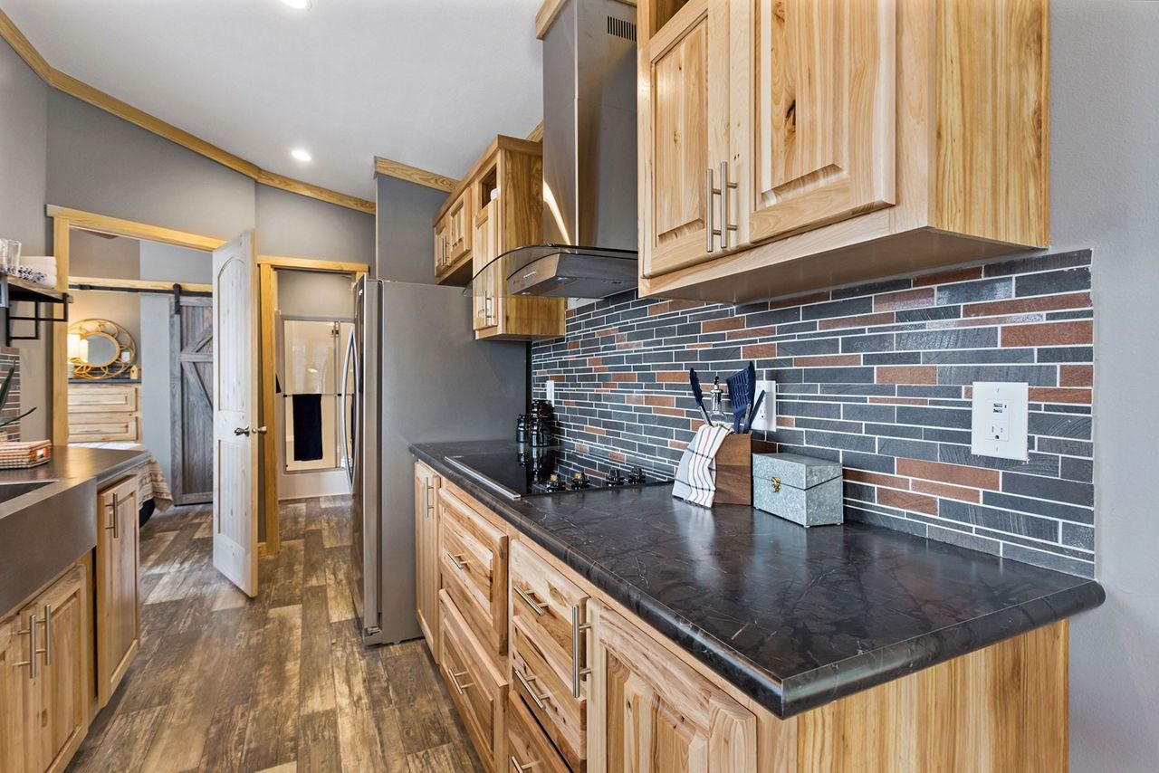 Modern kitchen with wood cabinets, black countertops, and a gray-blue tiled backsplash.