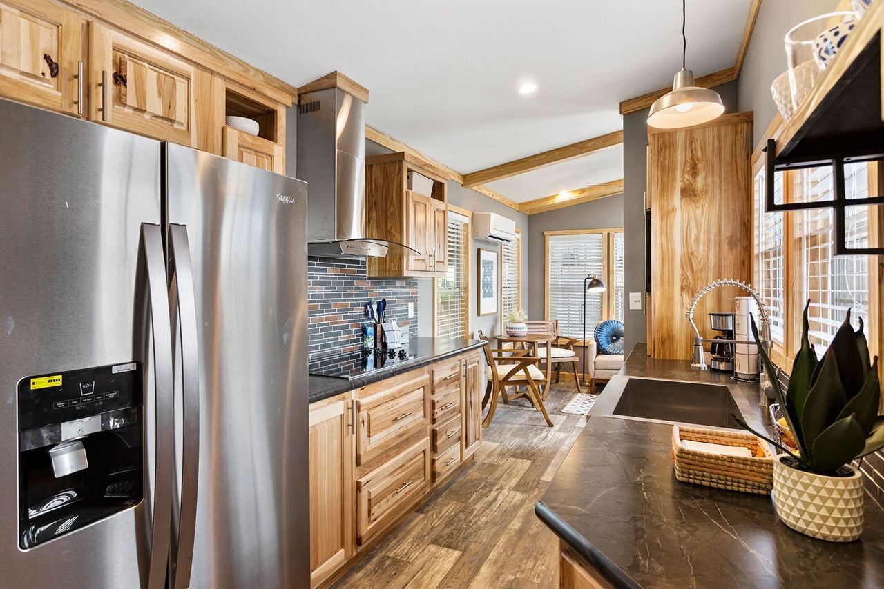 Bright, modern kitchen with stainless steel appliances, wood cabinetry, and a rustic dining nook by windows.