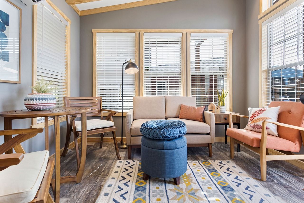 Cozy sunroom with beige sofa, orange chair, blue ottoman, and patterned rug by bright windows