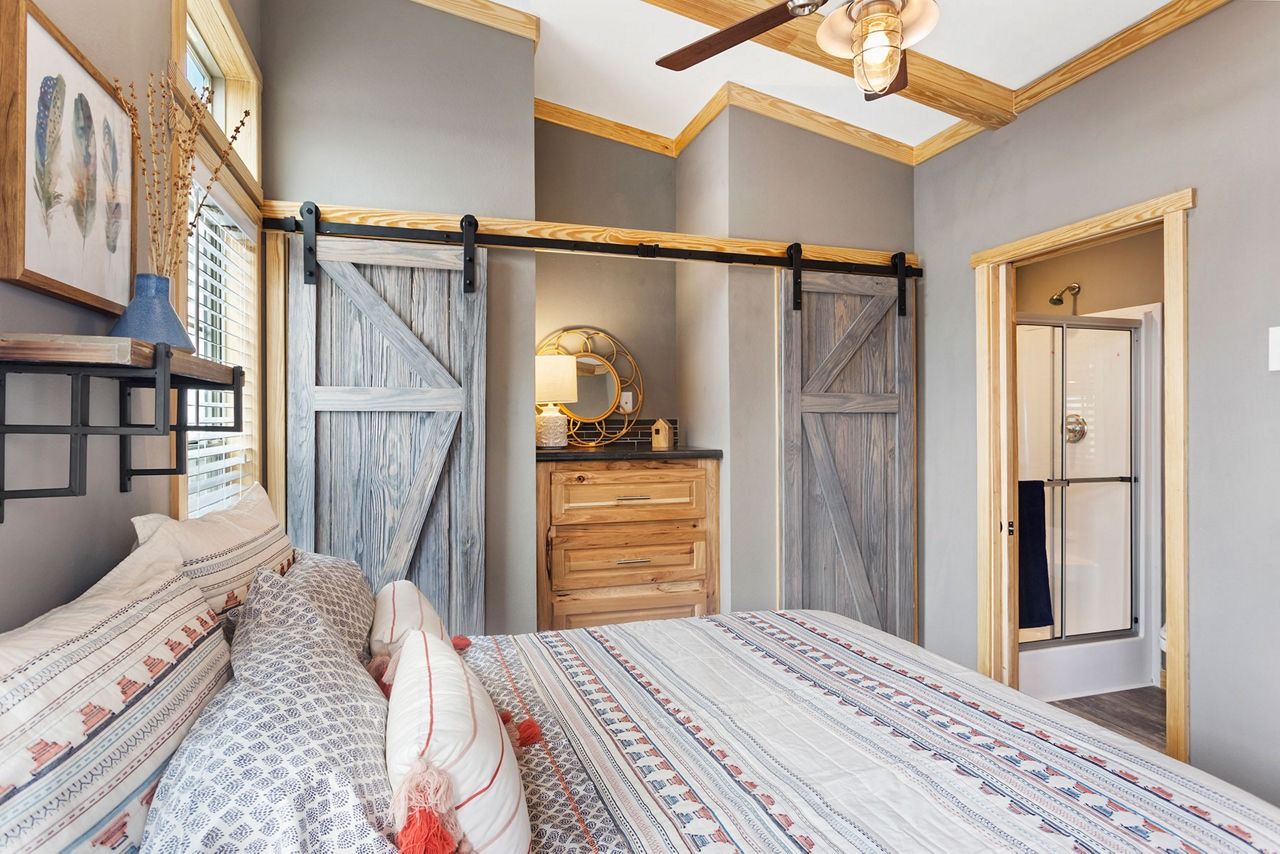 Rustic bedroom with sliding barn doors, patterned bedspread, and a dresser under a ceiling fan