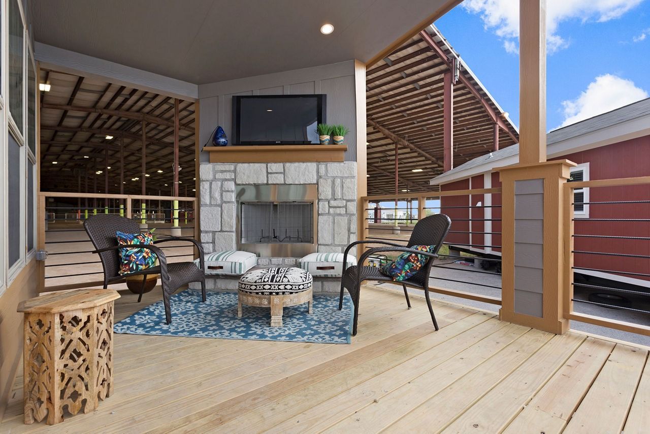 Covered outdoor patio with stone fireplace, wicker seating, and a blue rug on a wood deck.