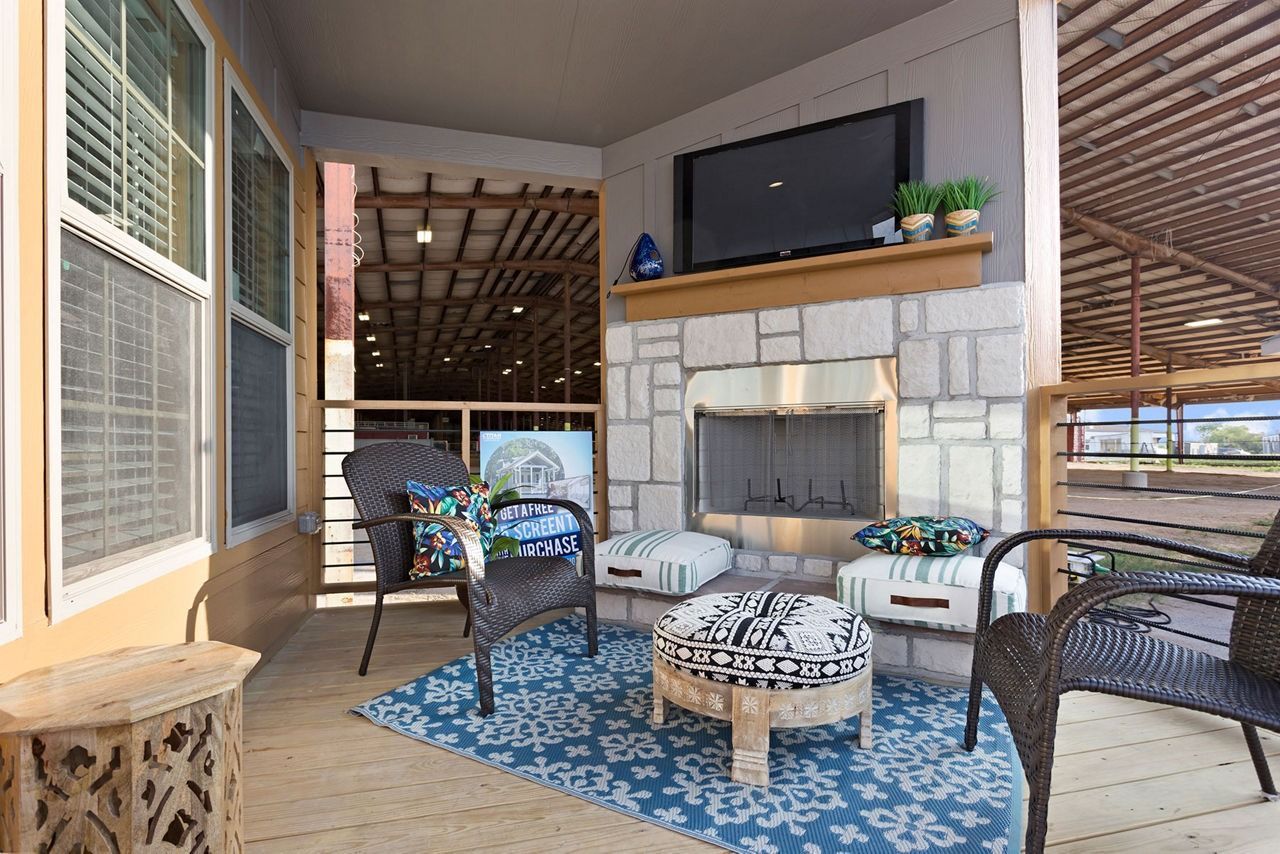 Covered patio with wicker seating, blue rug, stone fireplace, and wall-mounted TV