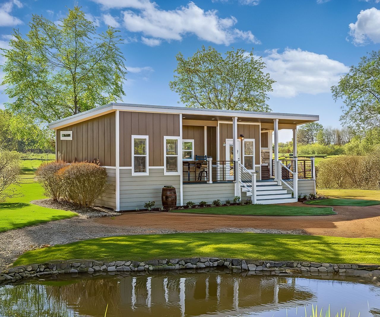 Small brown house with white porch by a pond under a blue sky