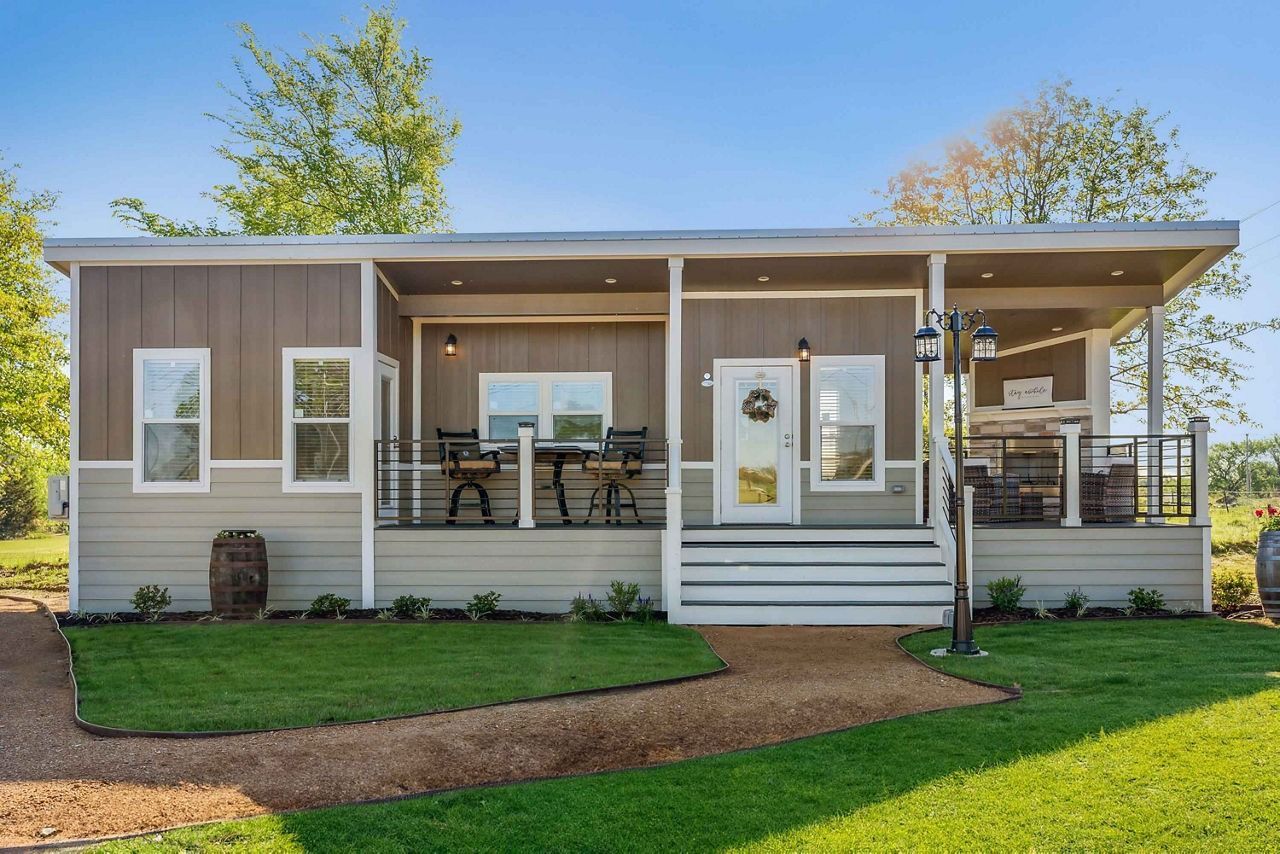 Small light-gray house with white trim, front porch, steps, and green lawn on a sunny day