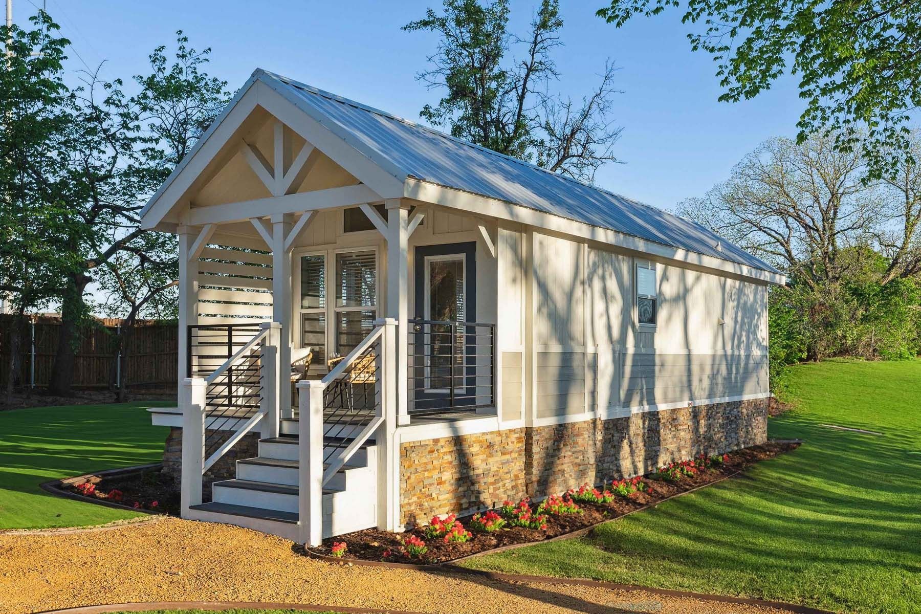 Small beige house with white trim, front porch, and stone base in a sunny yard