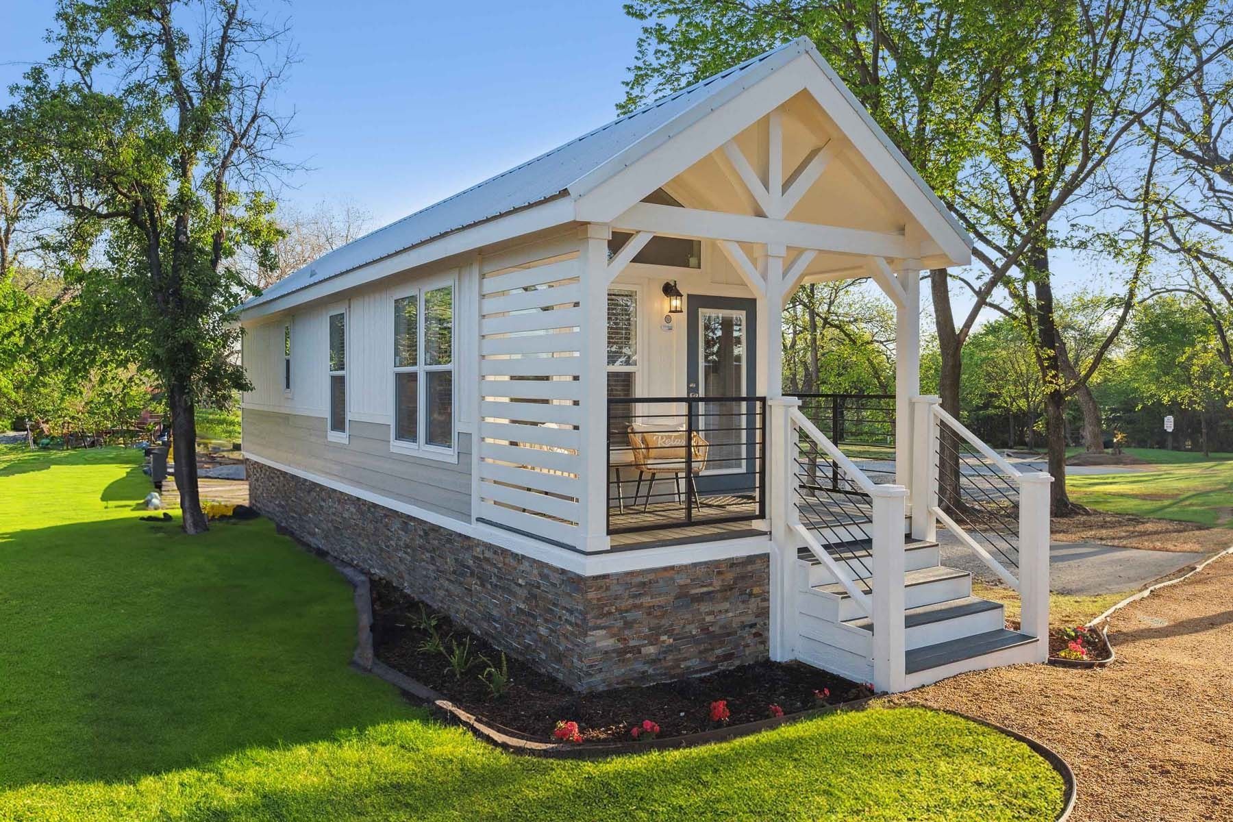 White porch-style tiny house with front steps on a sunny green lawn