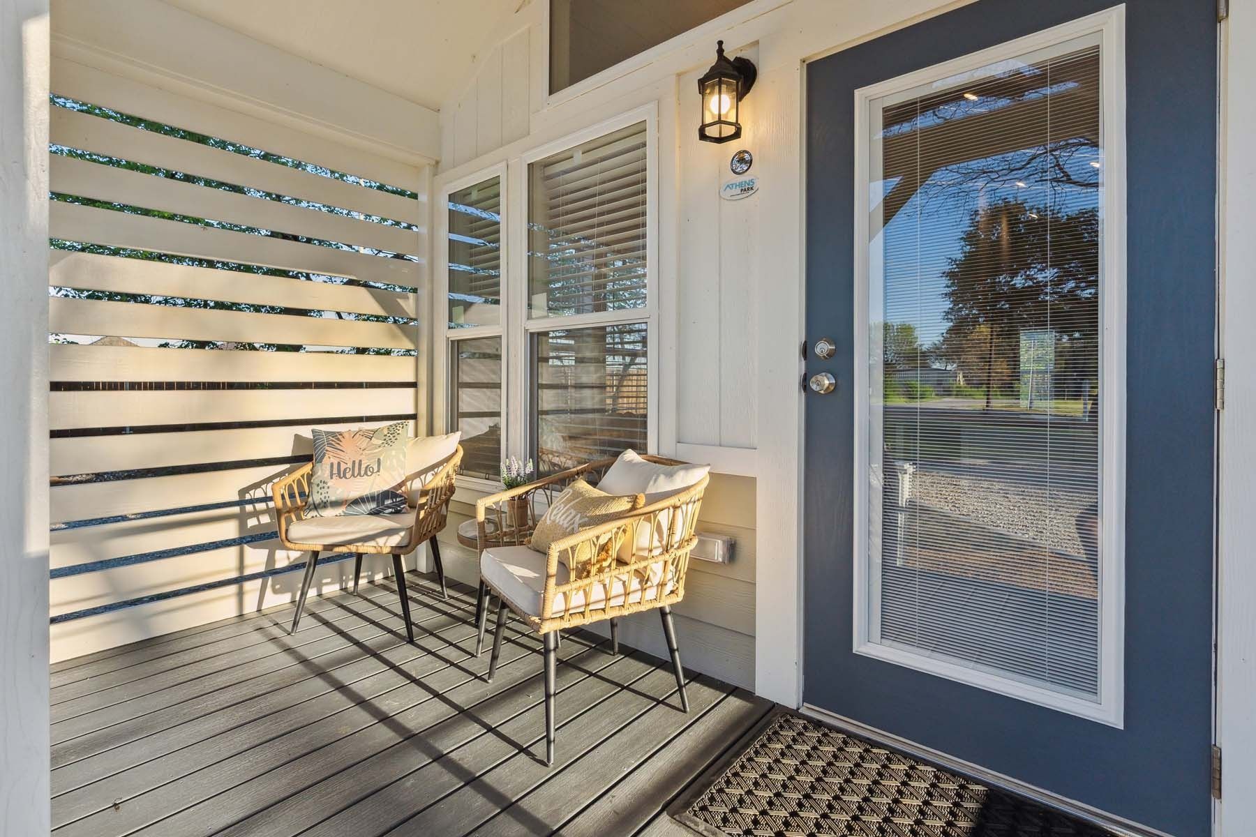 Front porch with two cushioned chairs, a blue door, and slatted privacy screen in warm sunlight