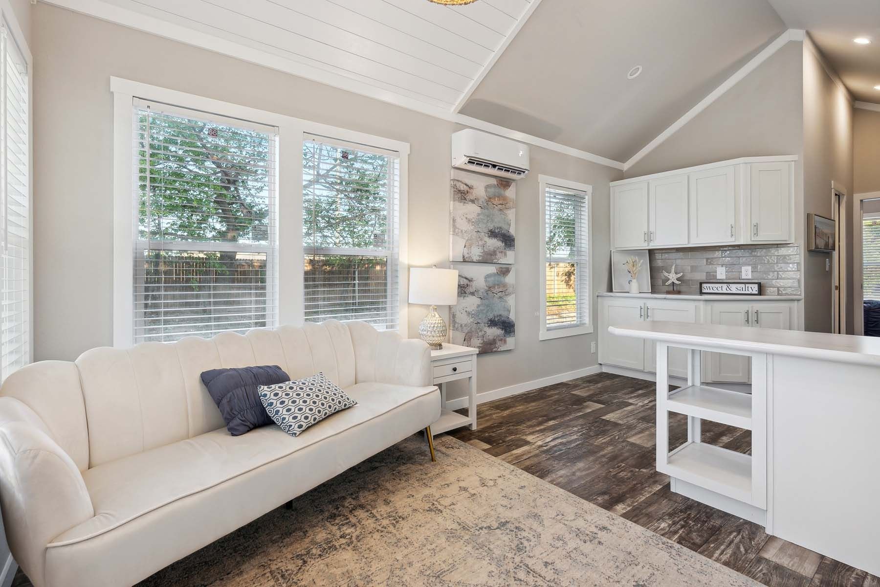Bright modern living room and kitchen with white sofa, island, and large windows