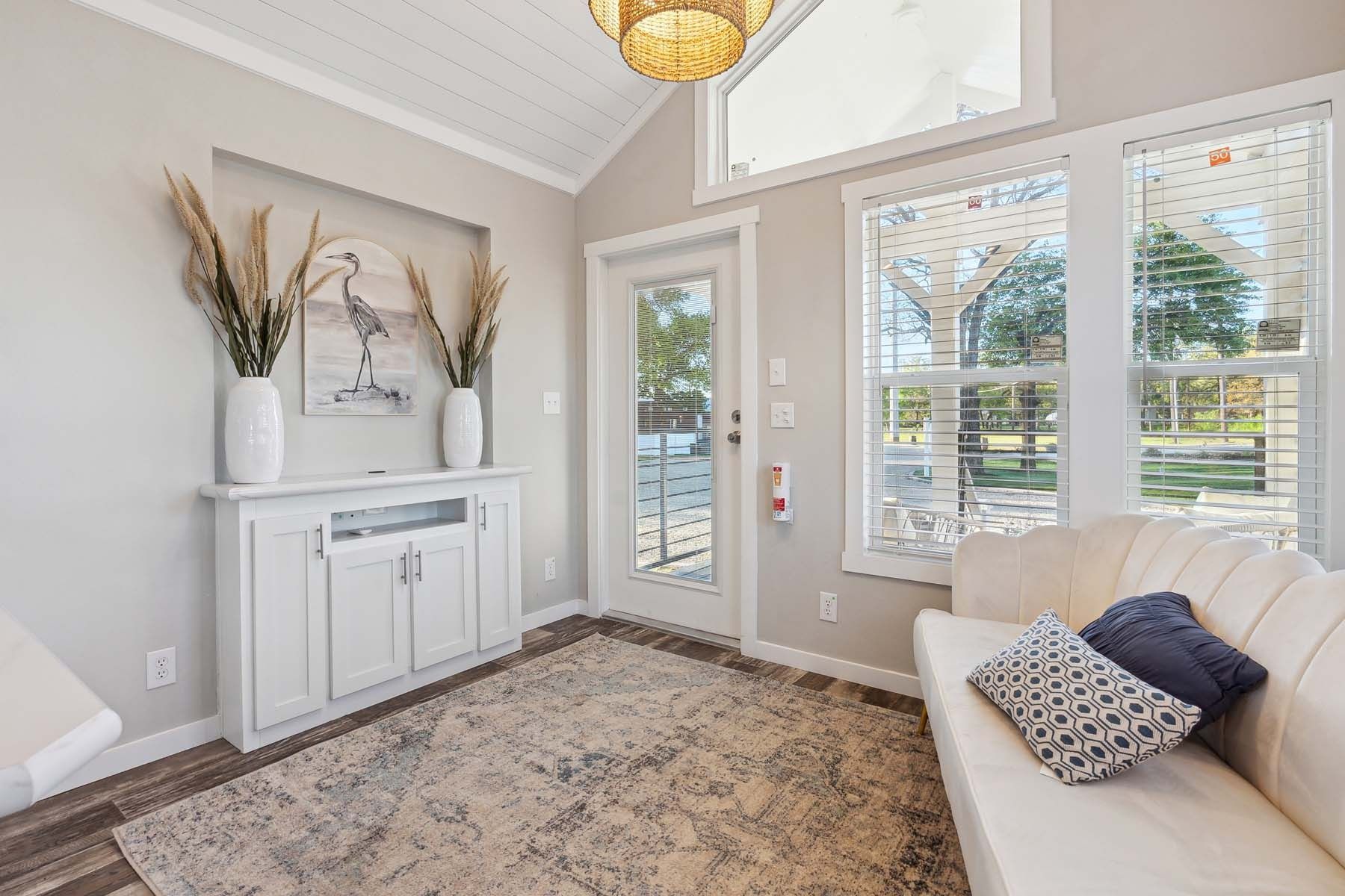 Bright entryway with white cabinets, large windows, patterned rug, and a light sofa.