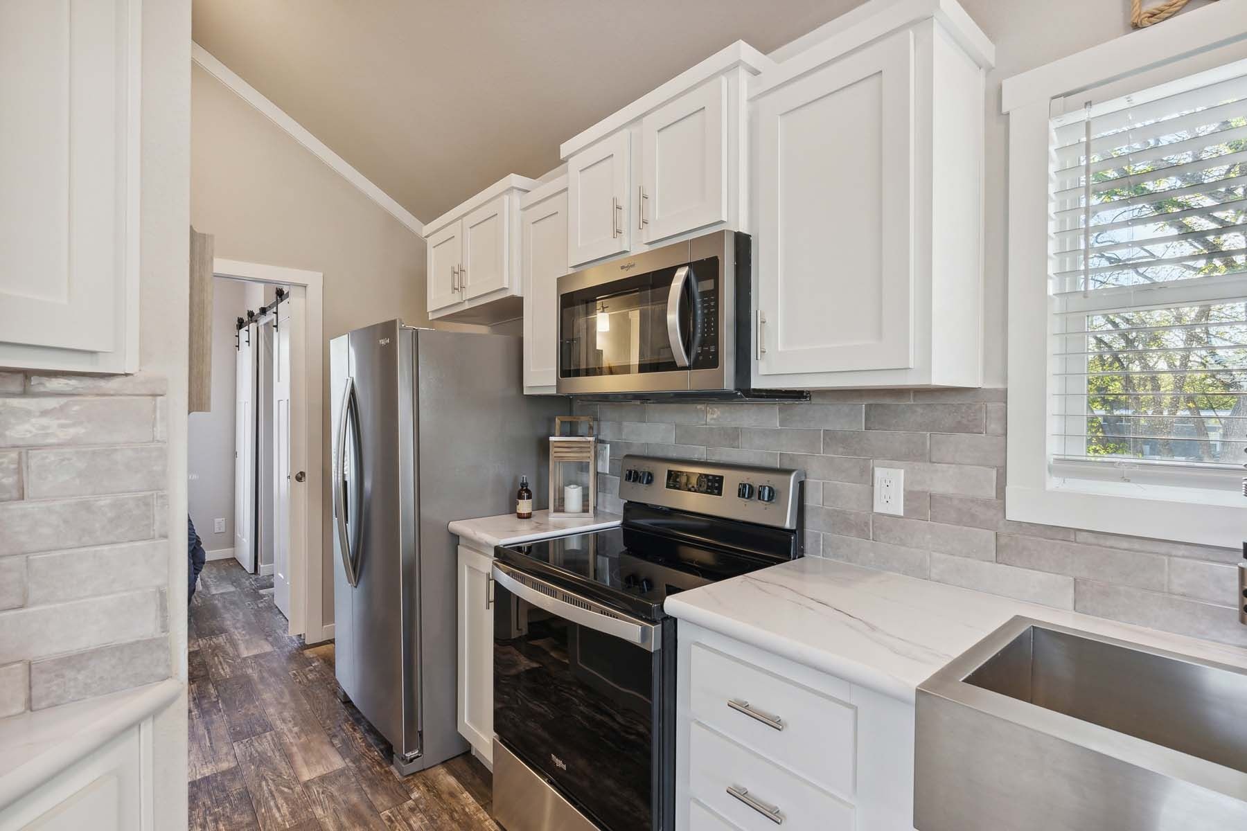 Bright modern kitchen with white cabinets, stainless steel appliances, and a window above the sink