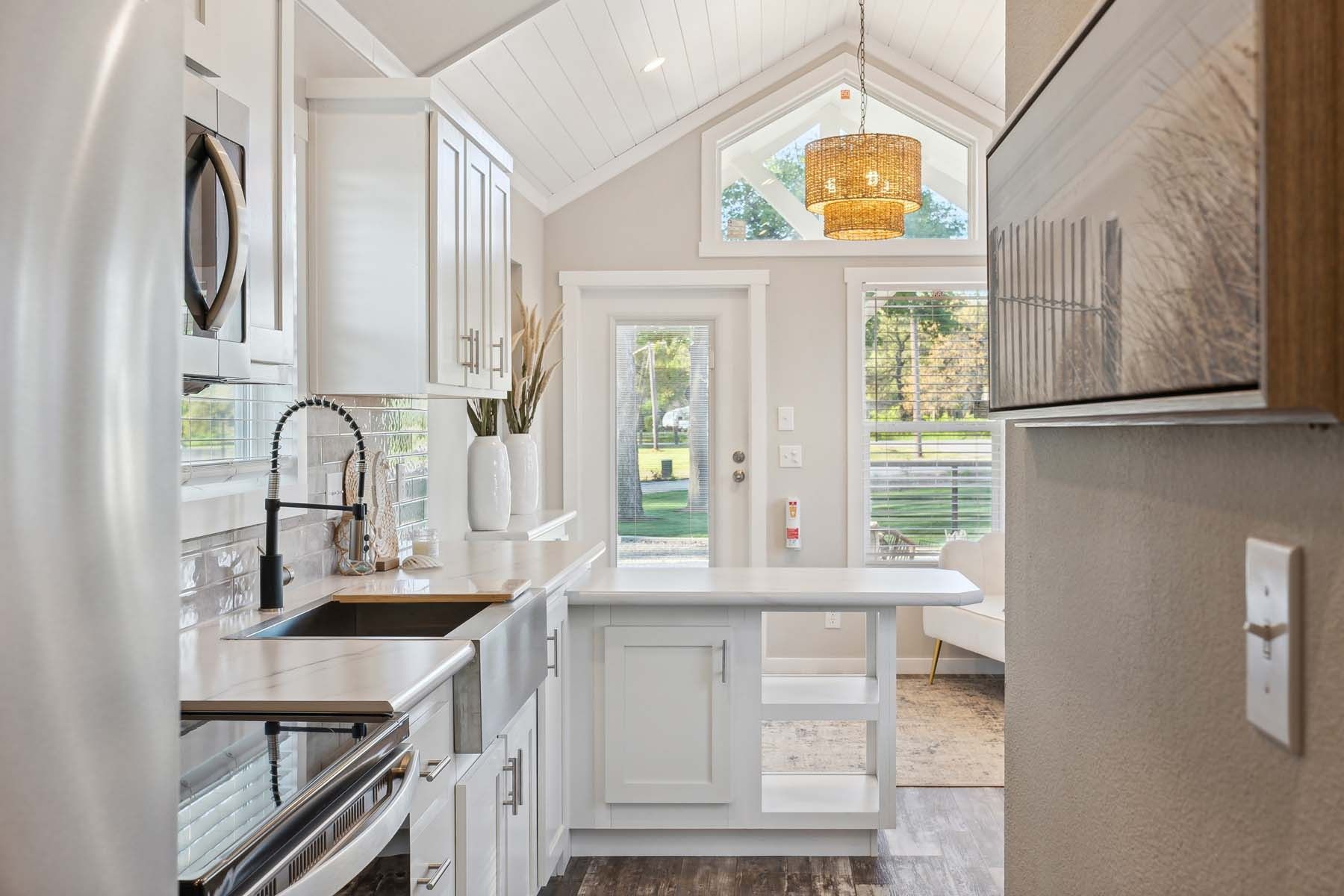 Bright narrow kitchen with white cabinets, stainless steel appliances, and a small dining nook by a glass door.