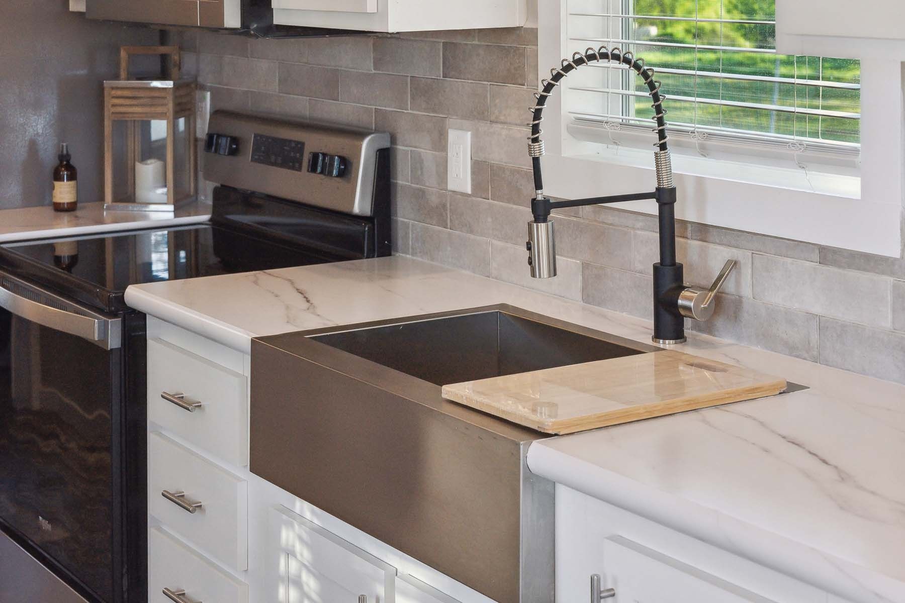 Modern kitchen with stainless steel appliances, white marble countertop, farmhouse sink, and black faucet by a window