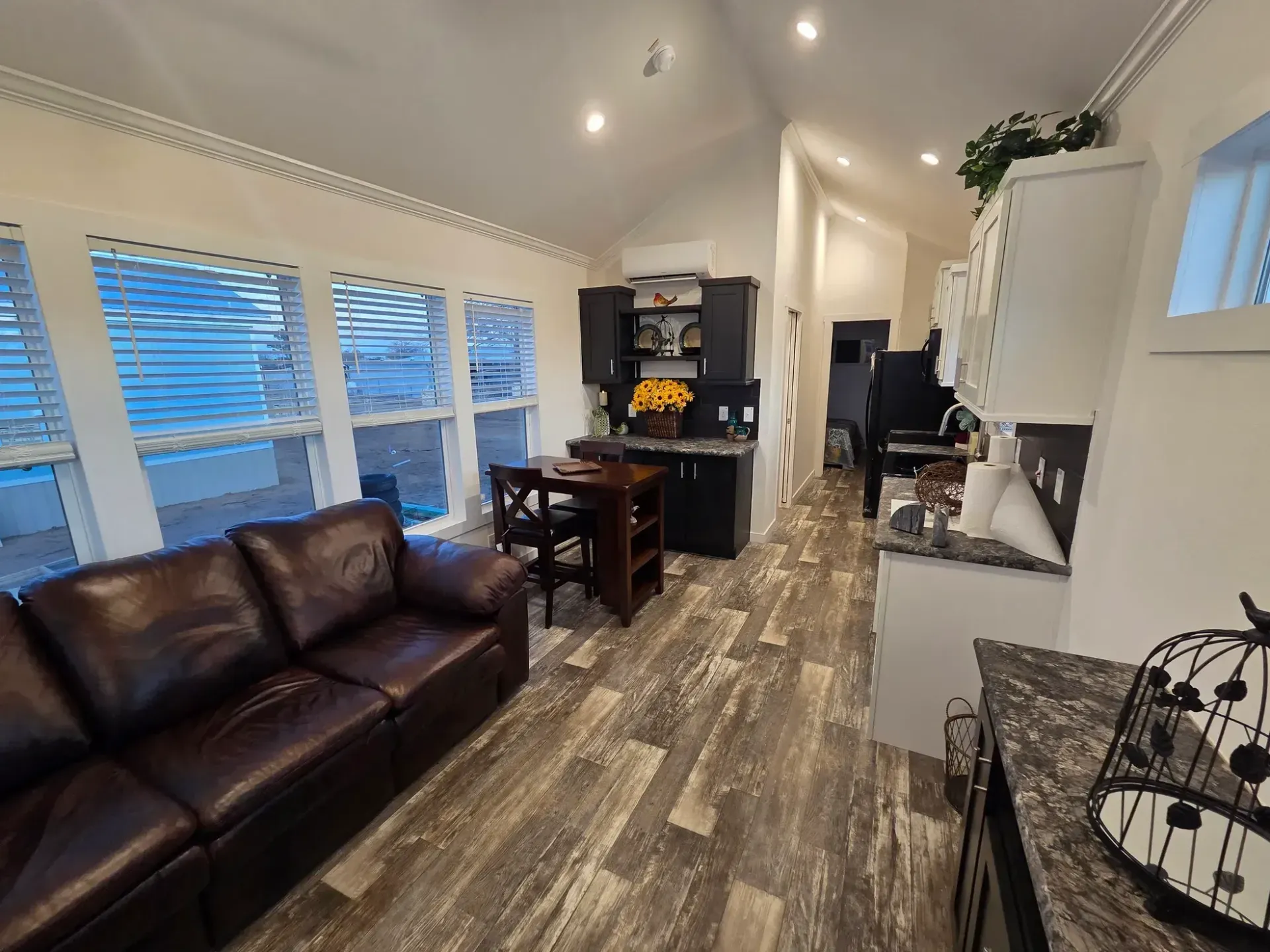 A modern, open-concept tiny house interior featuring a leather sofa, small dining table, and kitchenette.