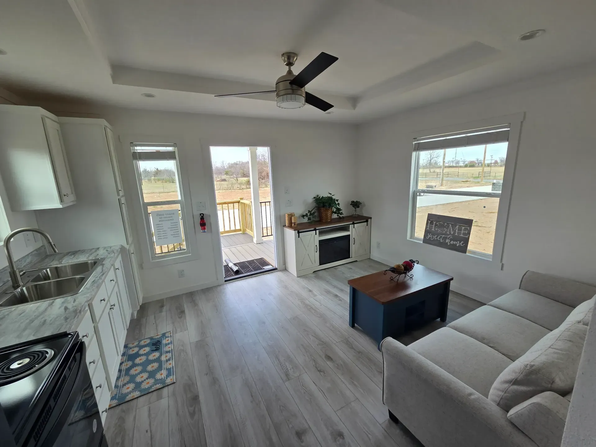 An open-concept living area with a kitchen, light wood flooring, a sofa, a coffee table, and a door leading to a porch.