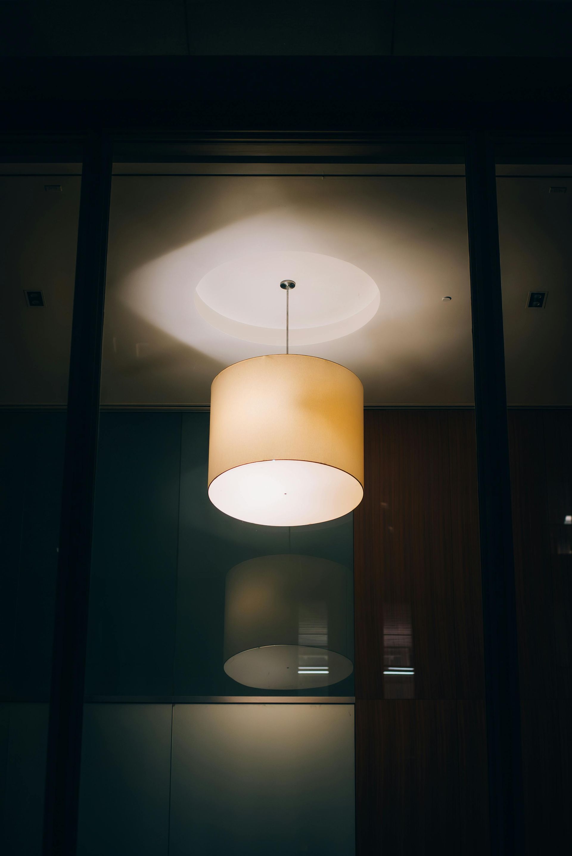 Warm beige pendant lamp glowing against a dark interior ceiling and wall.