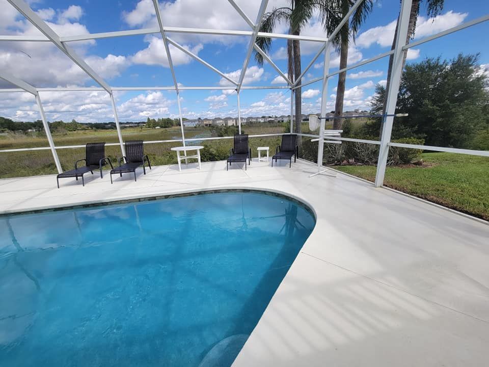 A large swimming pool is surrounded by chairs and a screened in area.