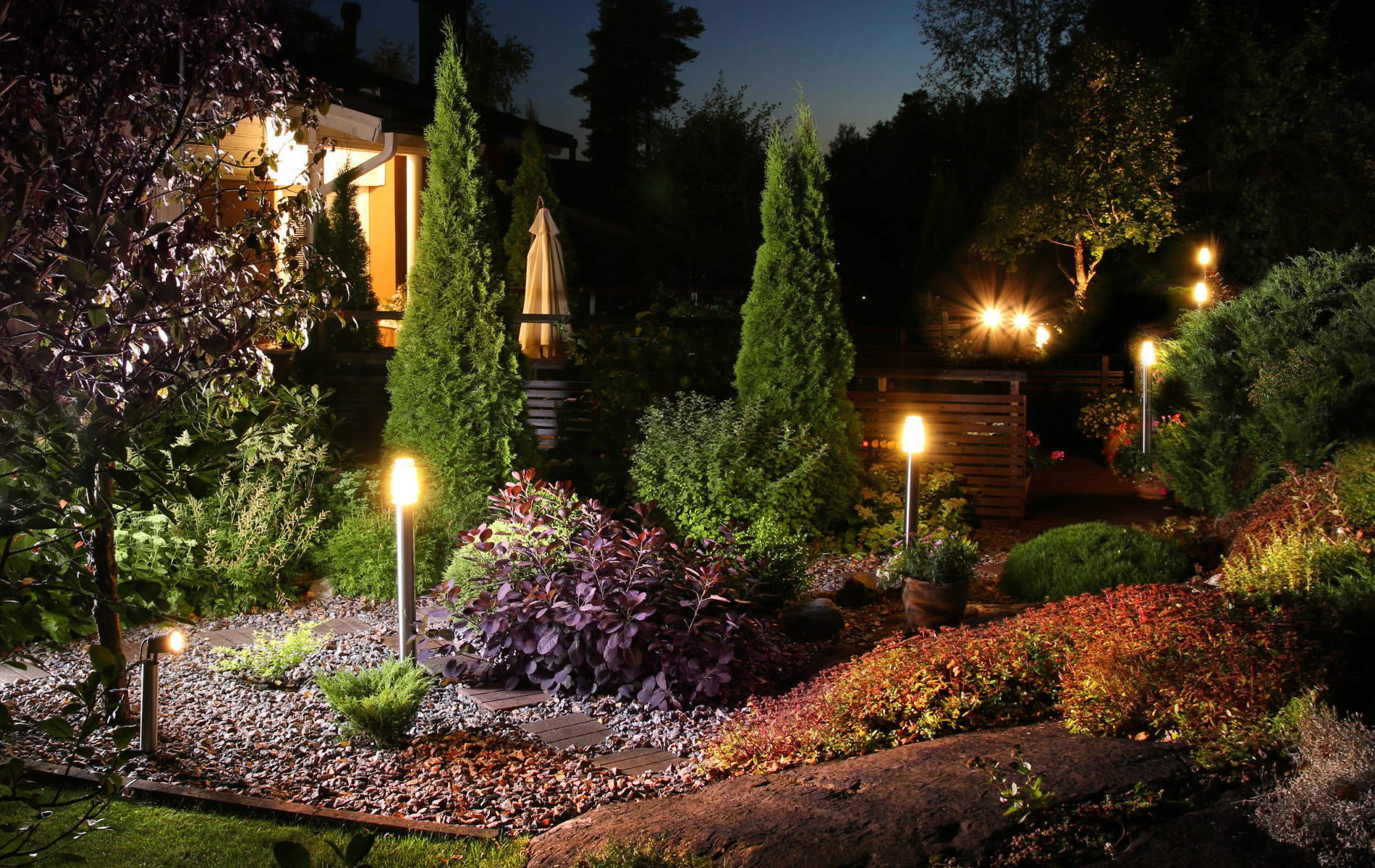 A garden is lit up at night with a house in the background