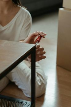 A woman is sitting on the floor fixing a table with a screwdriver.
