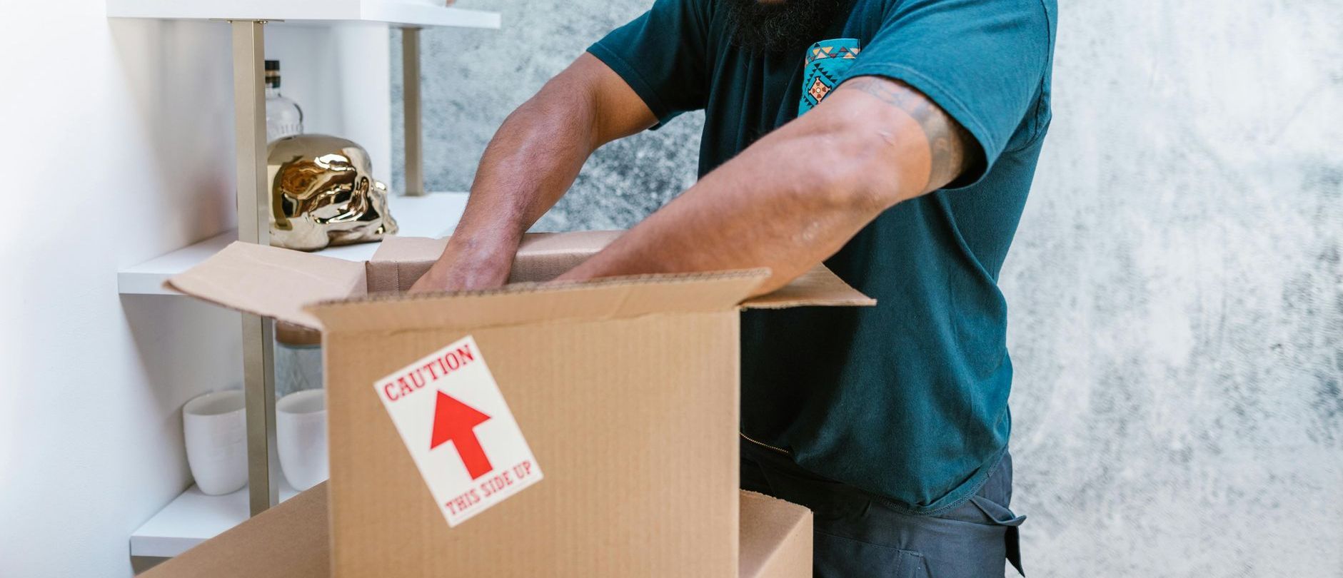 A man is packing a cardboard box in a room.