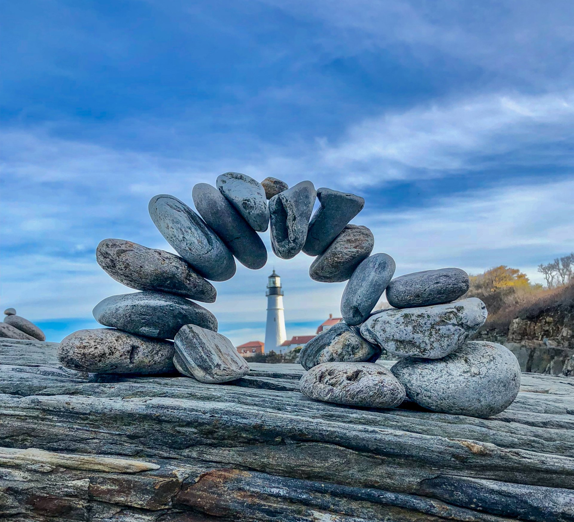river rocks balanced in an arc, white lighthouse in background symbolizing marketing approach of  The Syt