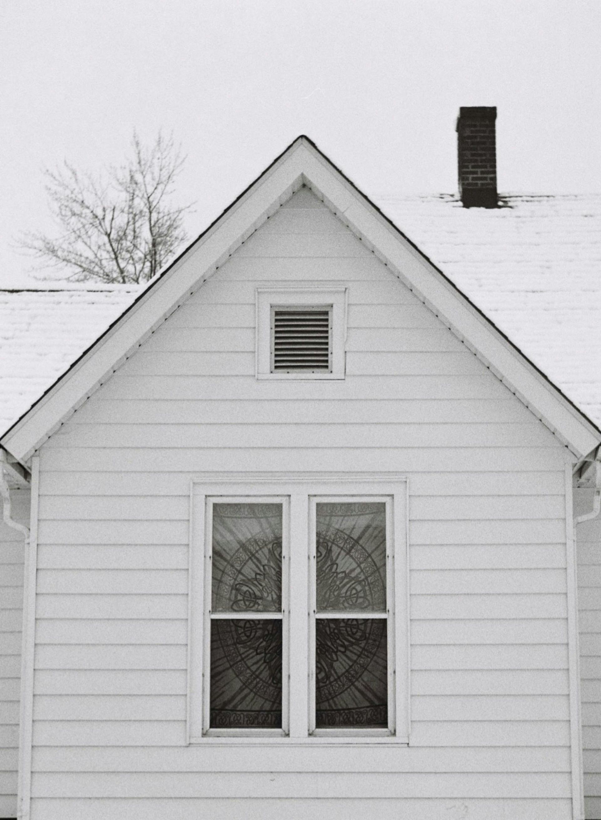 A white house with wood siding, a gabled roof and a chimney, covered in a light dusting of snow.