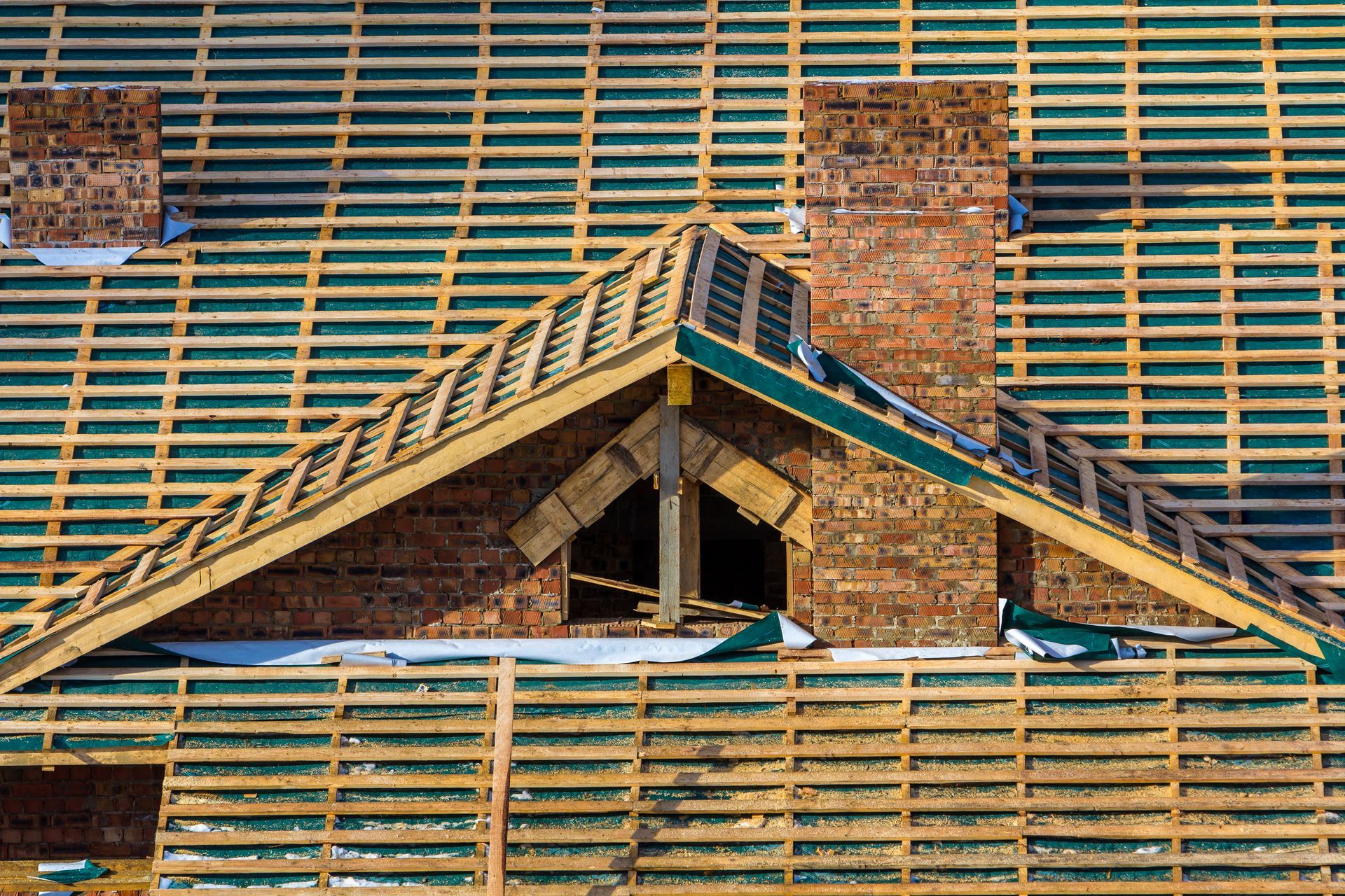 Overhead view of a roof under construction with visible wooden framework, chimney, and a partially built gabled section.