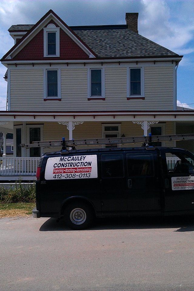 A black van parked in front of a two-story yellow house with a red roof. The van has a business logo.