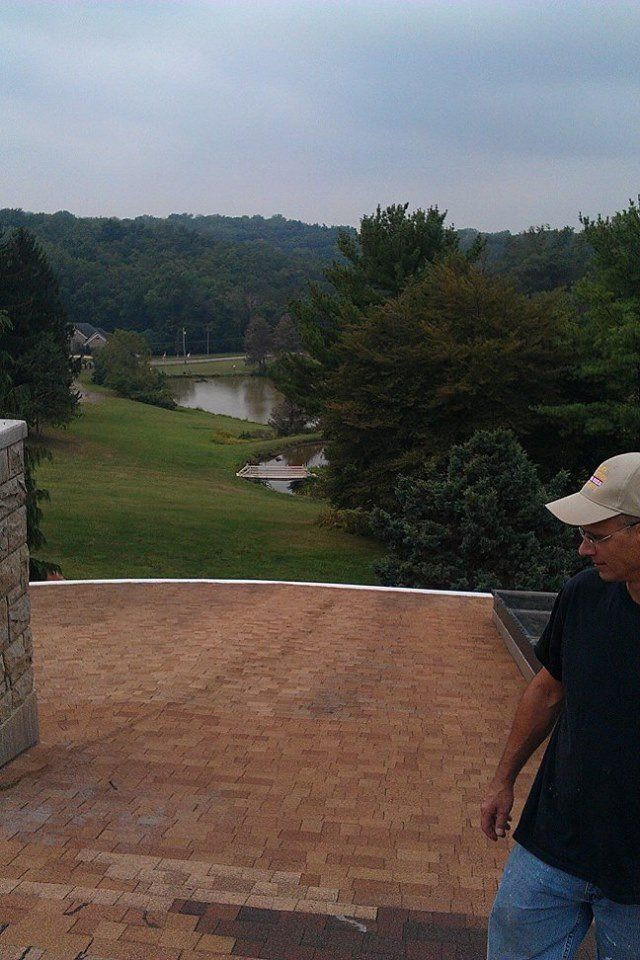 A man in a baseball cap is standing on a roof overlooking a lake.