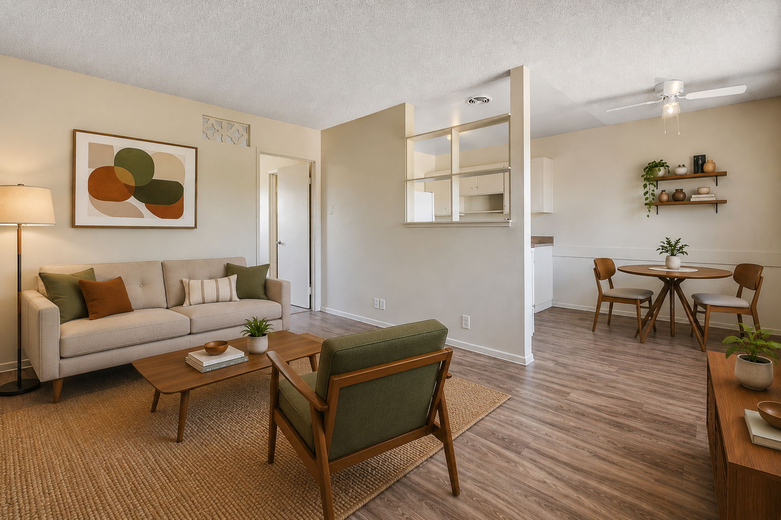 Bright living room with beige sofa, green chair, wall art, and small dining table by the window.